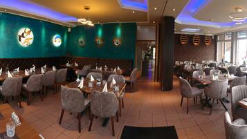 A restaurant with multiple dining areas, each with tables and chairs. There are decorative wall panels and a large window providing natural light.
