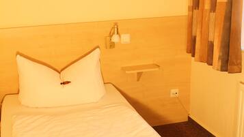 A hotel room with a bed, a nightstand, a wall-mounted lamp, and a painting above the bed.