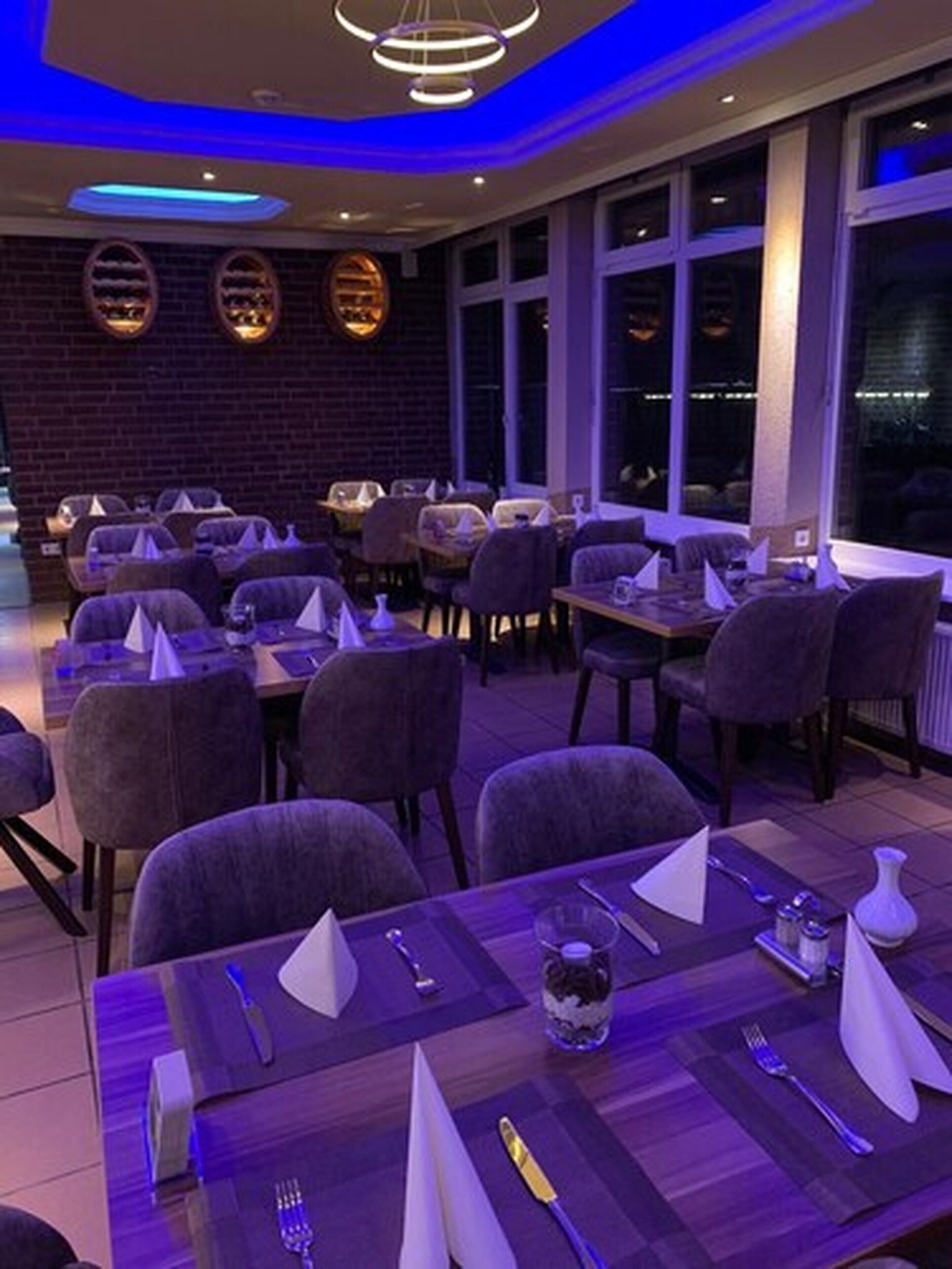 Un restaurante con mesas dispuestas para comer, con una decoración moderna que incluye una pared de ladrillo y grandes ventanales.