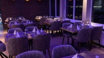 Un restaurante con mesas dispuestas para comer, con una decoración moderna que incluye una pared de ladrillo y grandes ventanales.