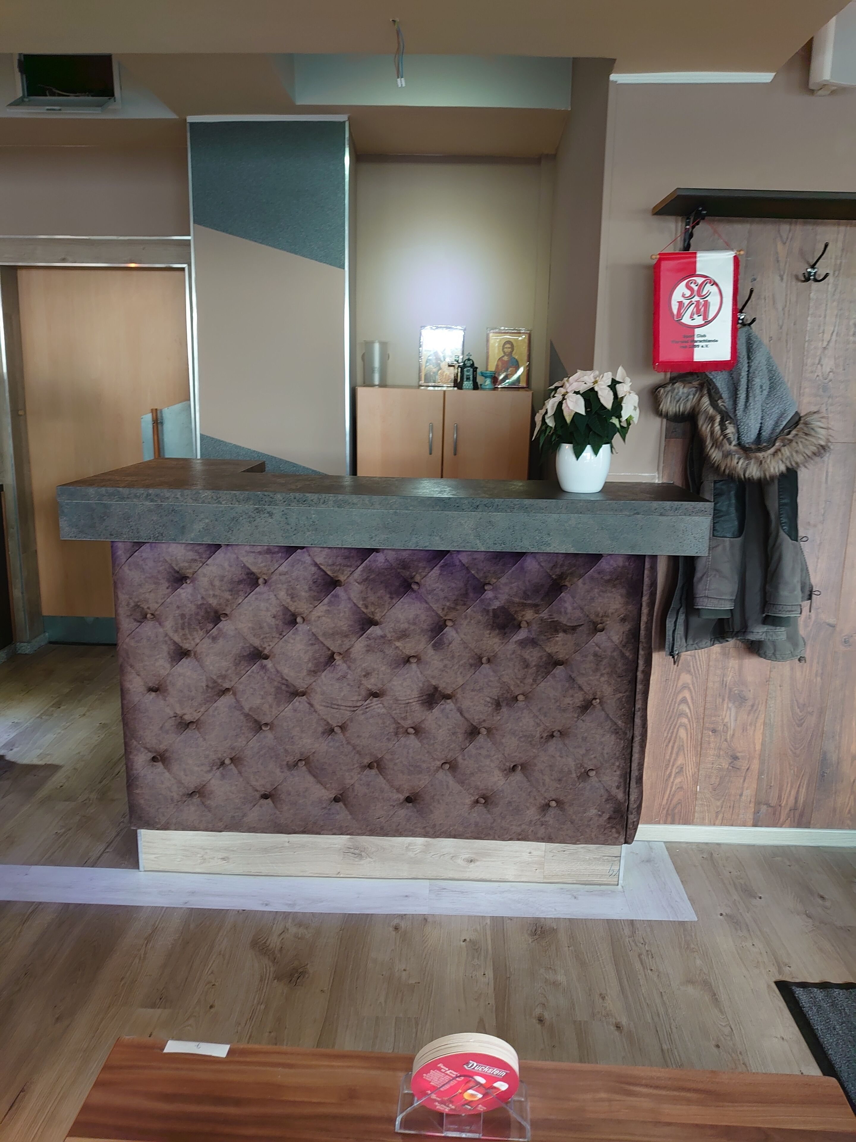A kitchen area with a marble countertop, a tufted brown upholstered bar, and a wooden cabinet with a red sign.