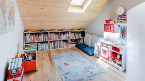 A cozy attic bedroom with a sloped ceiling, wooden beams, a skylight, a bookshelf, a play area with toys, and a small kitchenette. - Sumptuous house with patio (Paris)