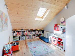 A cozy attic bedroom with a sloped ceiling, wooden beams, a skylight, a bookshelf, a play area with toys, and a small kitchenette. - Sumptuous house with patio (Paris)