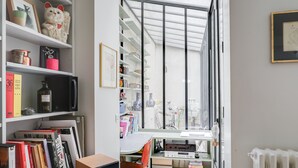 A modern room with a large window, a desk with a chair, and shelves filled with books and decorative items. - Sumptuous house with patio (Paris)