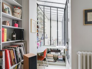 A modern room with a large window, a desk with a chair, and shelves filled with books and decorative items. - Sumptuous house with patio (Paris)
