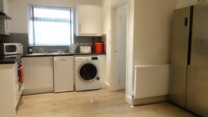 A compact kitchen with a washing machine, a microwave, and a refrigerator. - Grand Airport Ensuites (West Drayton)