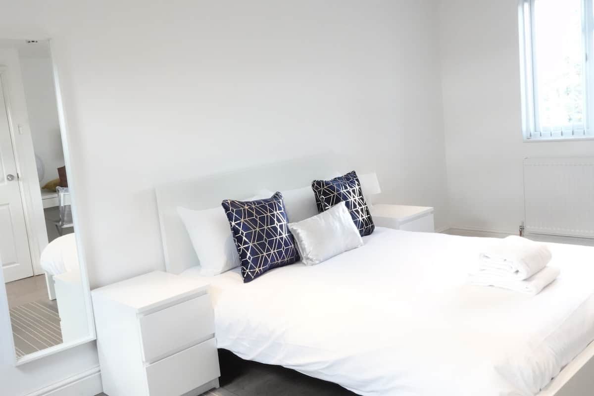 Ein modernes Hotelzimmer mit einem ordentlich bezogenen Bett, weißen Nachttischen und einem großen Spiegel.