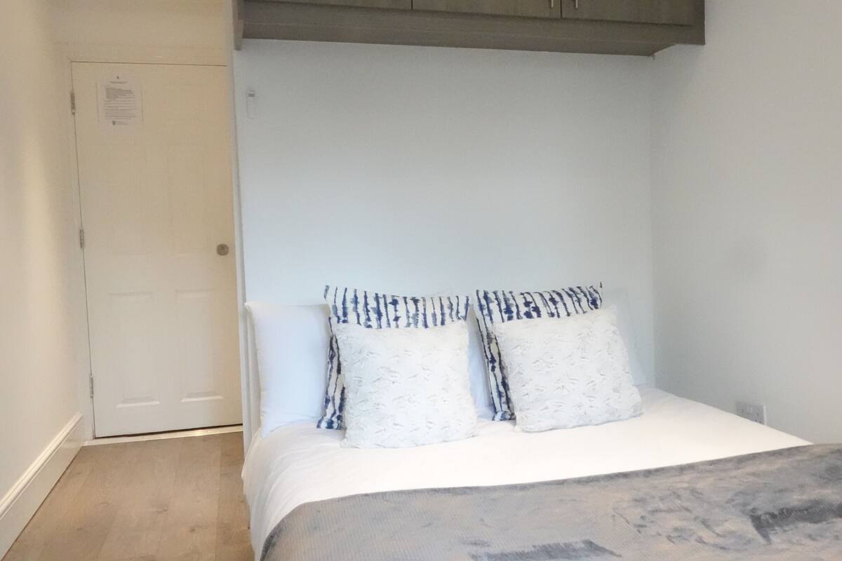 Ein kleines, ordentlich eingerichtetes Schlafzimmer mit einem Bett, zwei Kissen und einem Nachttisch.