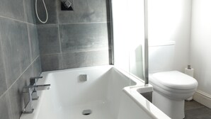 A modern bathroom with a white bathtub, a glass shower enclosure, and a toilet. - Grand Airport Ensuites (West Drayton)
