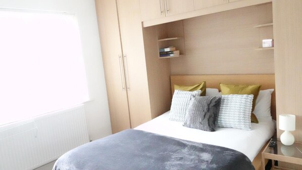 A bedroom with a bed, pillows, a bedside table, a lamp, and a window.