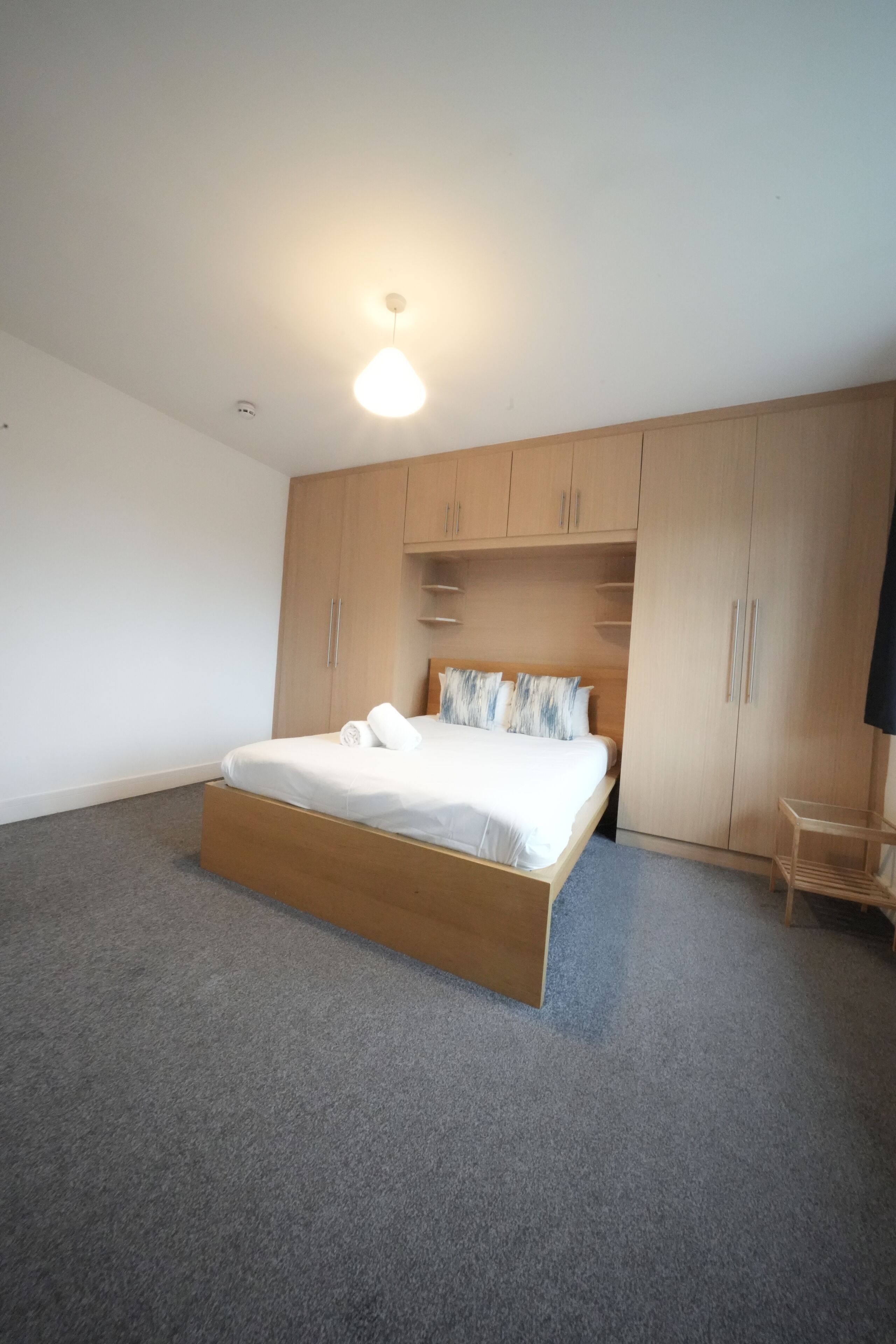 A bedroom with a bed, wooden wardrobe, and a small table.