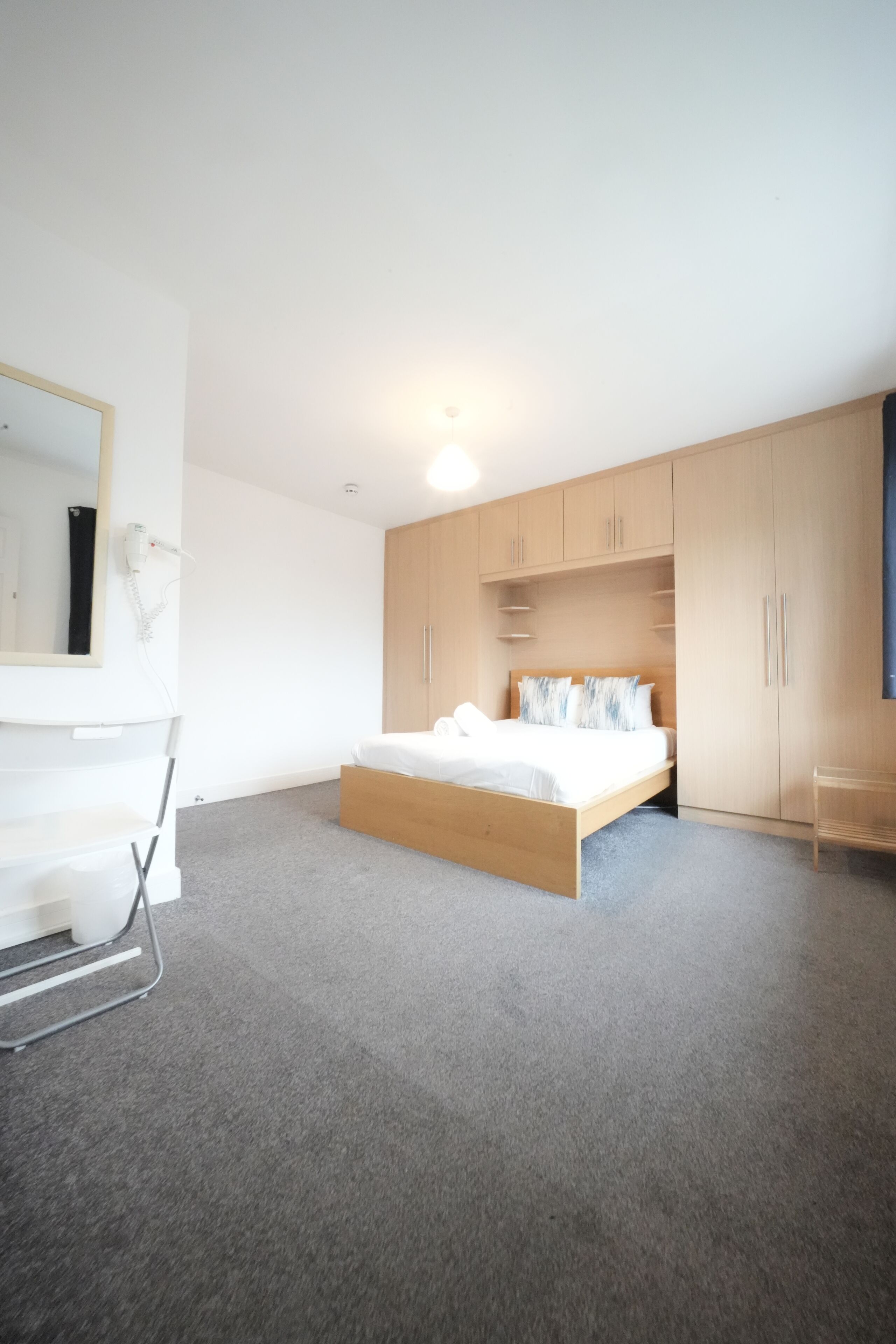 Une chambre moderne avec un lit en bois, un grand miroir et des armoires encastrées.