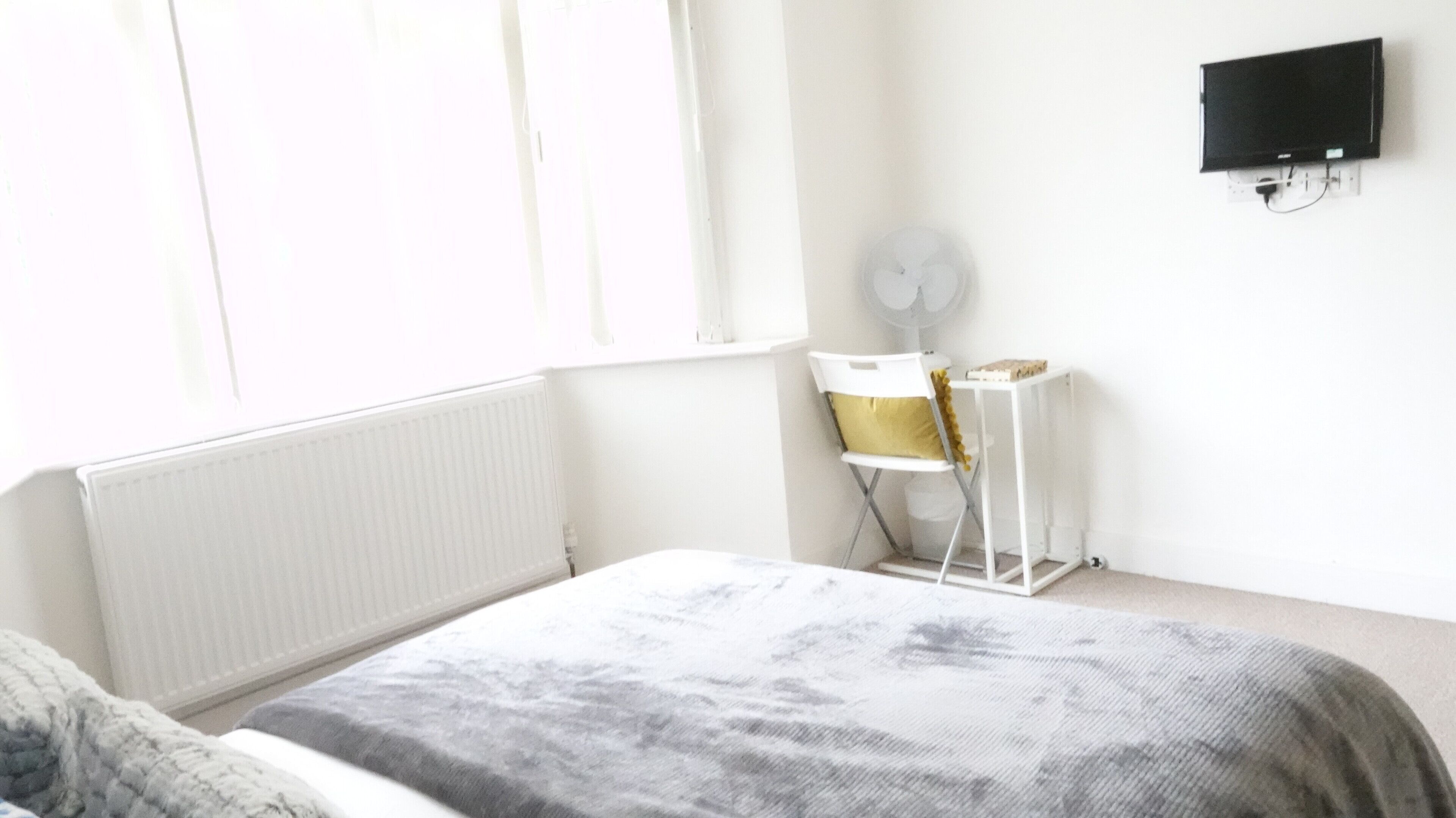 Un dormitorio con cama, escritorio, silla, radiador y televisor fijado a la pared.