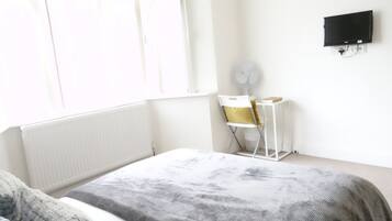 Un dormitorio con cama, escritorio, silla, radiador y televisor fijado a la pared.