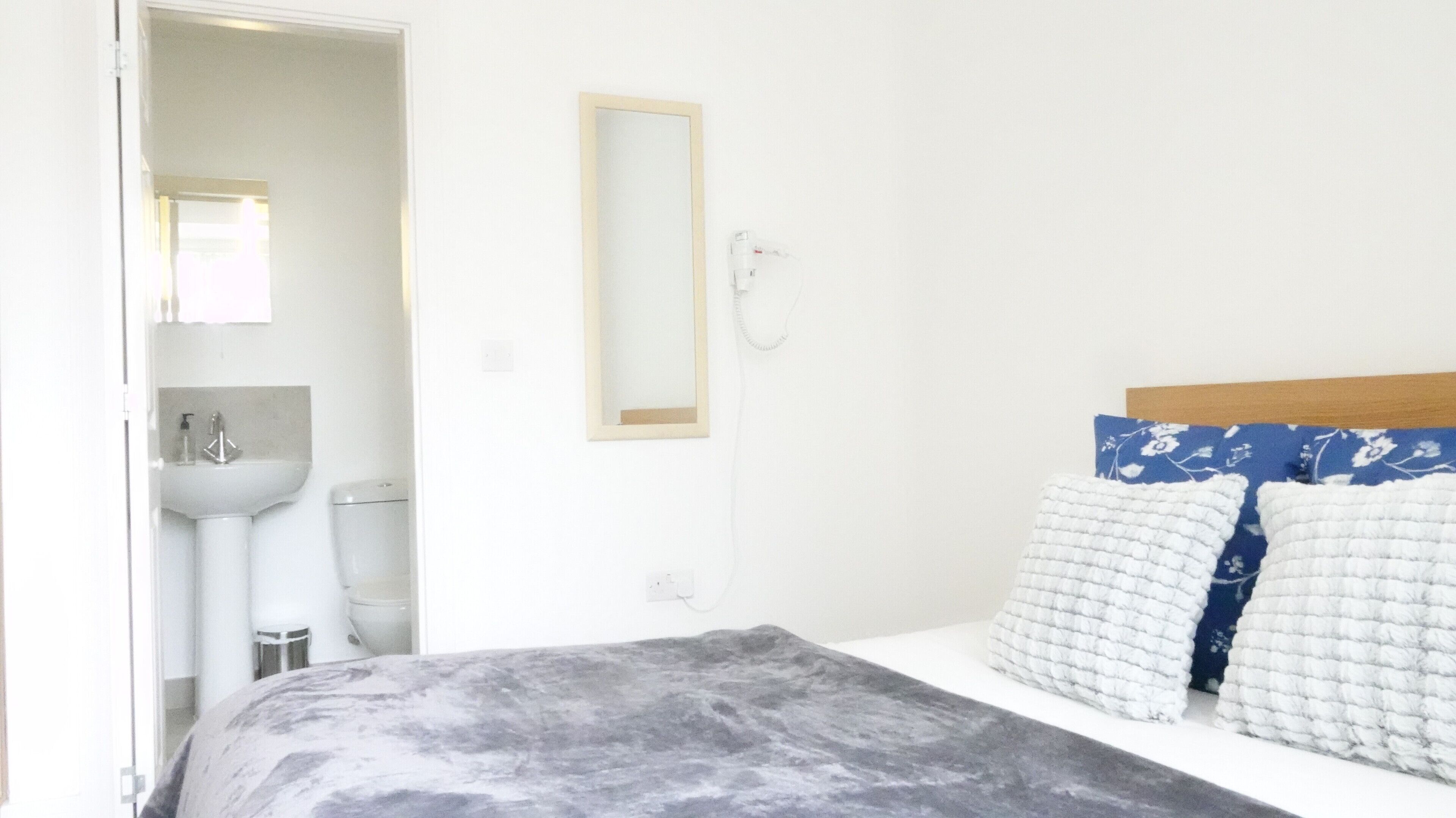 Een slaapkamer met een bed, nachtkastje, spiegel, wastafel en toilet.