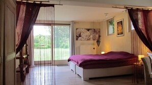 A bedroom with a bed, a window with curtains, a radiator, and a wall-mounted lamp. - A spacious and quiet villa in the heart of Flanders, near Bruges and the sea! (Maldegem)