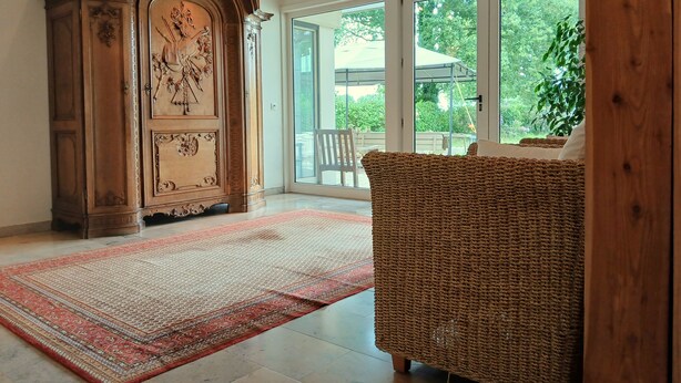 A spacious room with a large wooden cabinet, a woven sofa, and a patterned rug. - A spacious and quiet villa in the heart of Flanders, near Bruges and the sea! (Maldegem)
