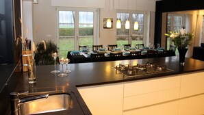 A modern kitchen with a large island, stainless steel appliances, and a dining area with a view of the outdoors. - A spacious and quiet villa in the heart of Flanders, near Bruges and the sea! (Maldegem)