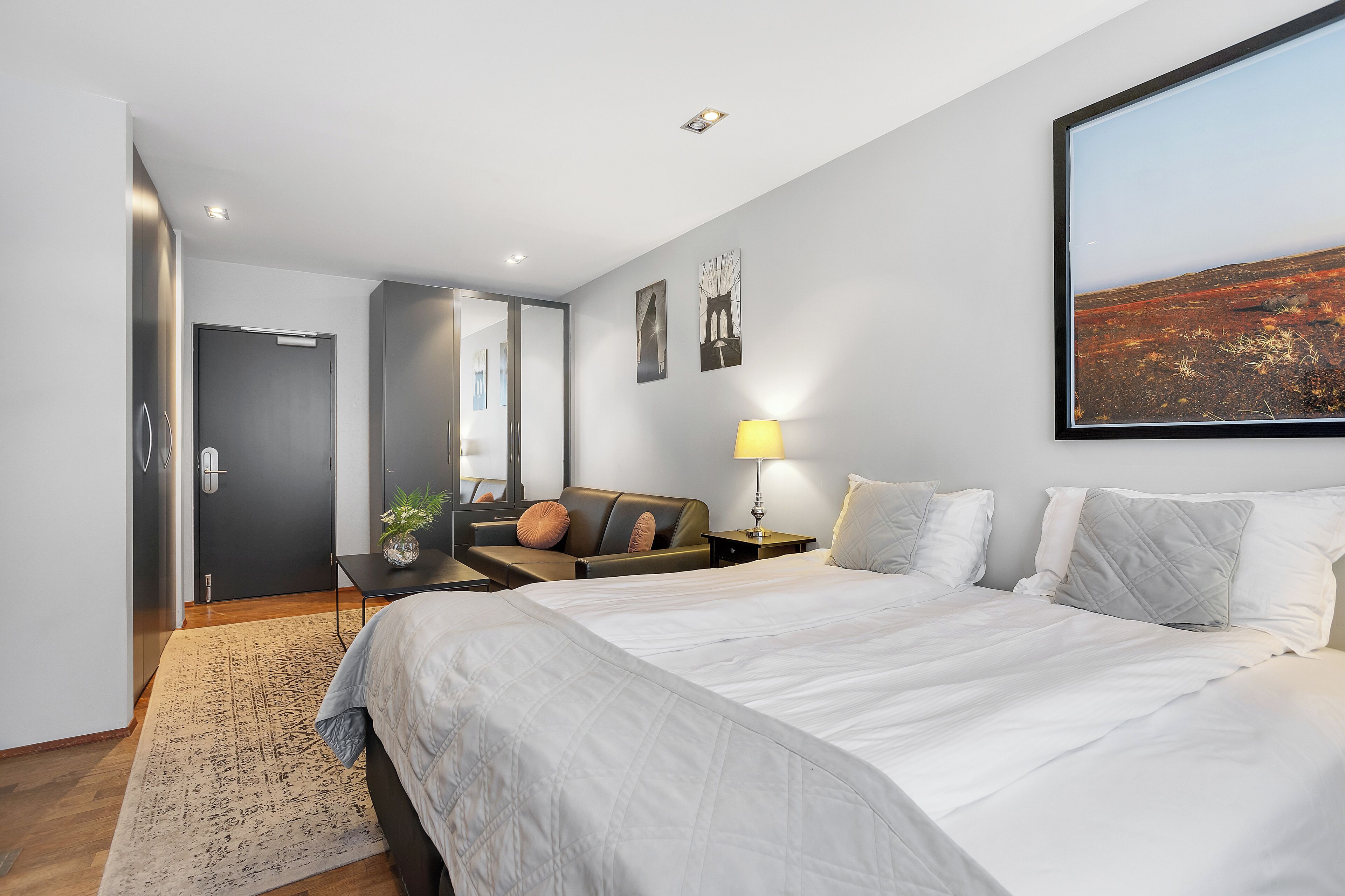 Una habitación de hotel moderna con una cama grande, un escritorio, una silla y una mesita de noche con una lámpara.