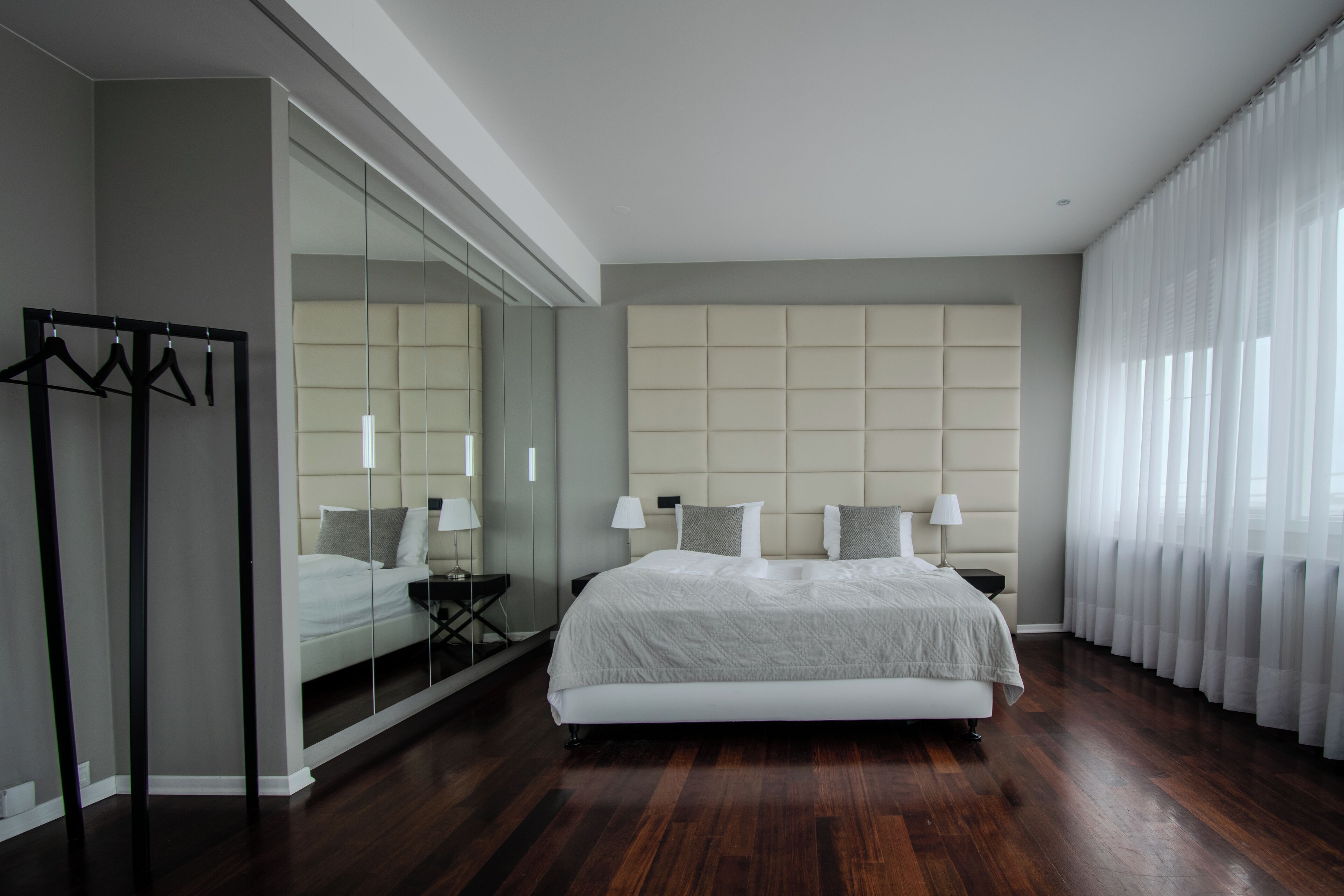 A modern bedroom with a large bed, a mirror, and a wardrobe.