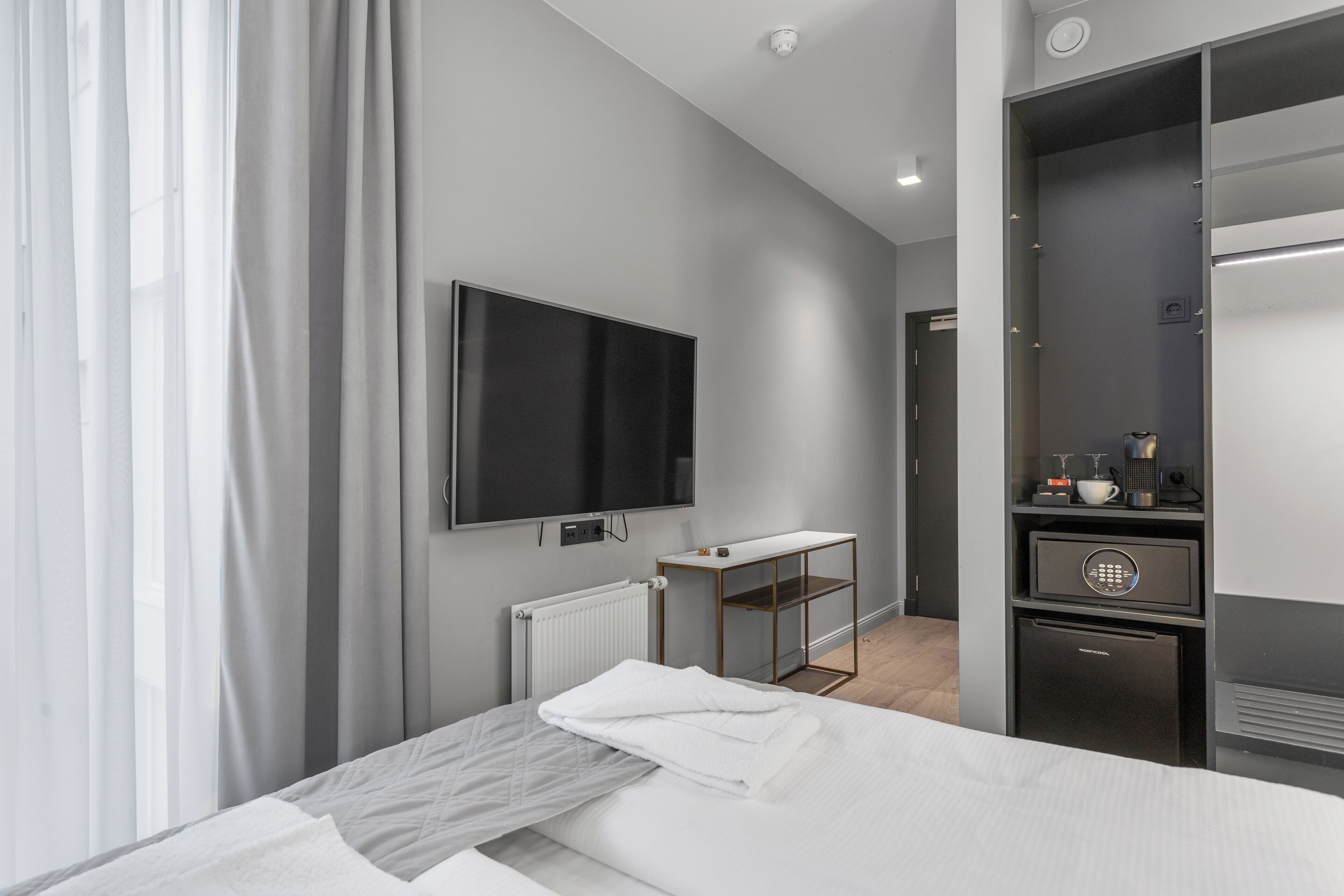 Una habitación de hotel moderna con una cama, un televisor de pantalla plana, un mini refrigerador, una cafetera y un vestidor.