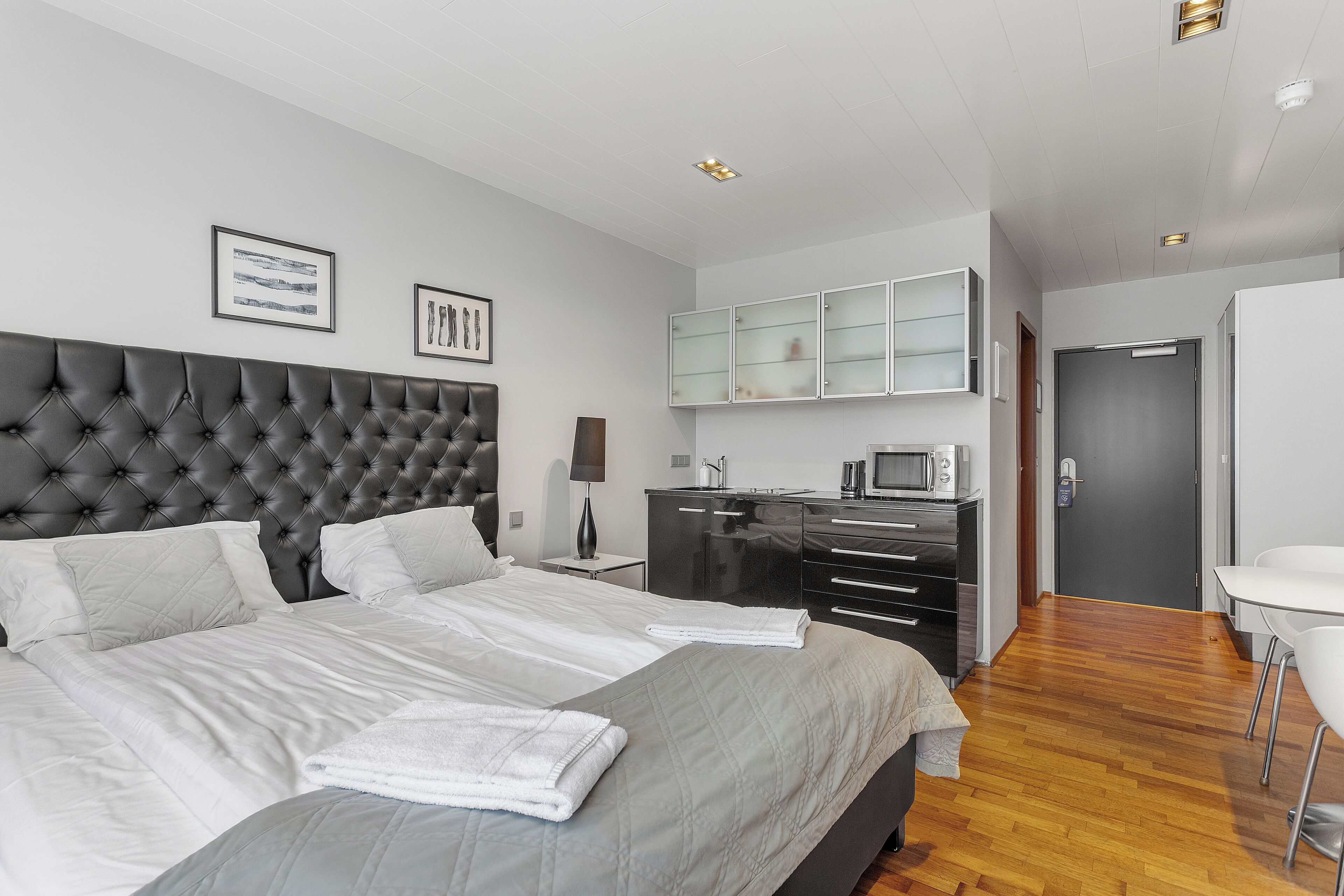 A modern hotel room with a large bed, a desk with a computer, a microwave, and a small kitchenette.