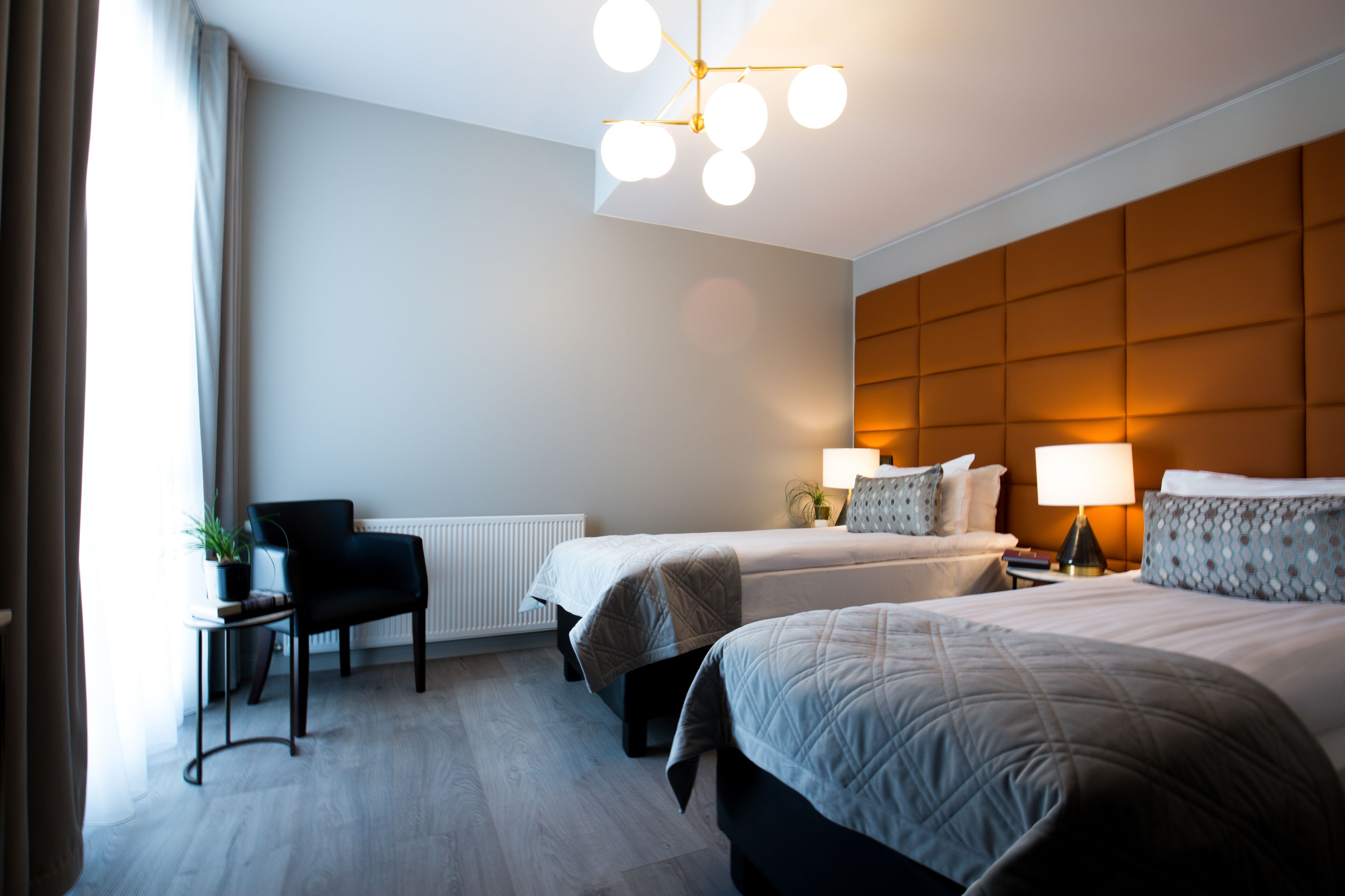 Une chambre d’hôtel avec deux lits, une chaise, une table avec une plante et un luminaire moderne au plafond.