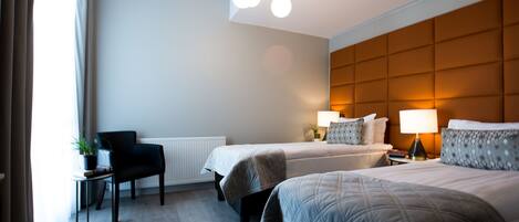 A hotel room with two beds, a chair, a table with a plant, and a modern ceiling light fixture.