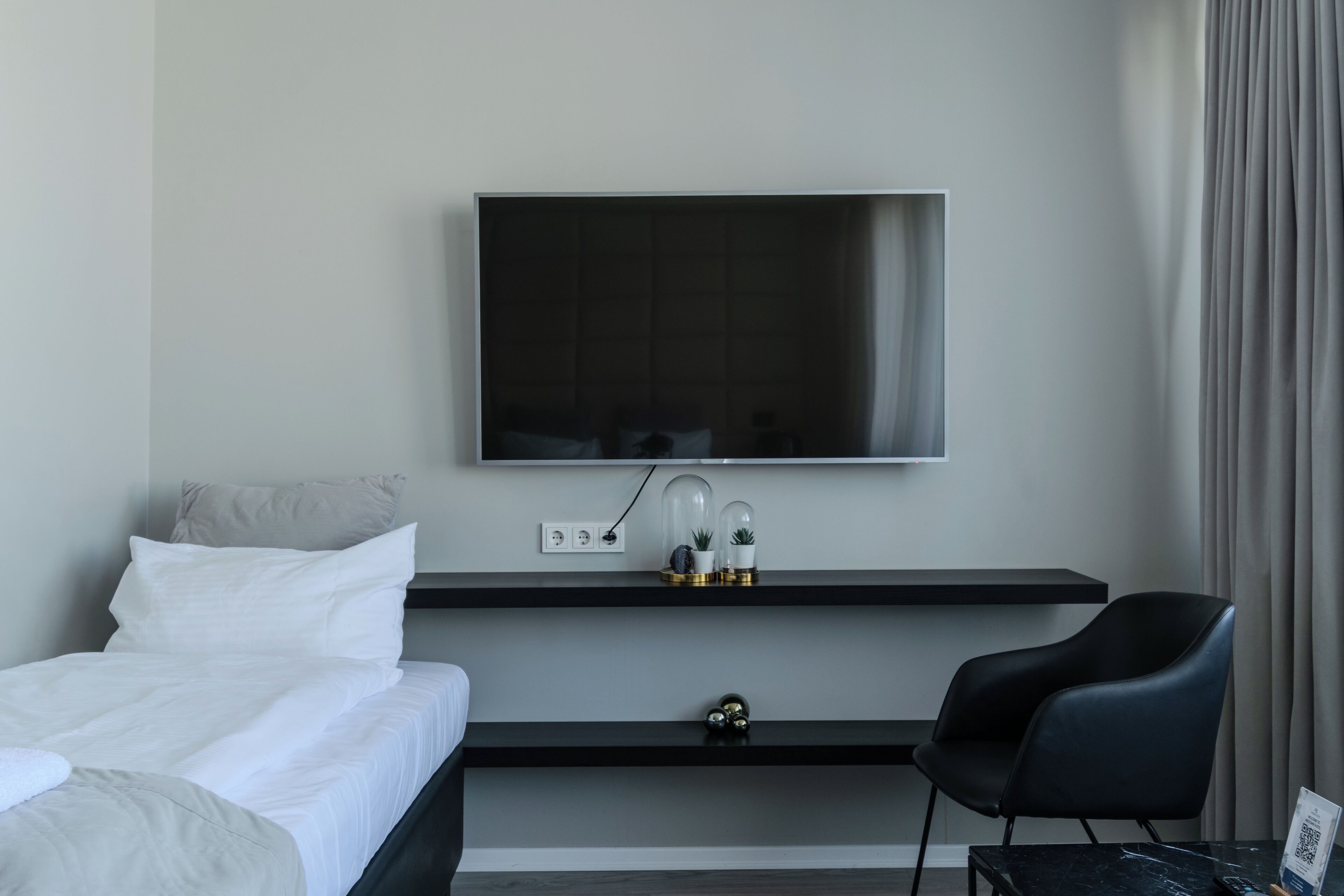 Ein modernes Hotelzimmer mit einem Bett, einem schwarzen Sessel, einem flachbildfernseher an der Wand und einem kleinen Tisch mit einer Lampe.