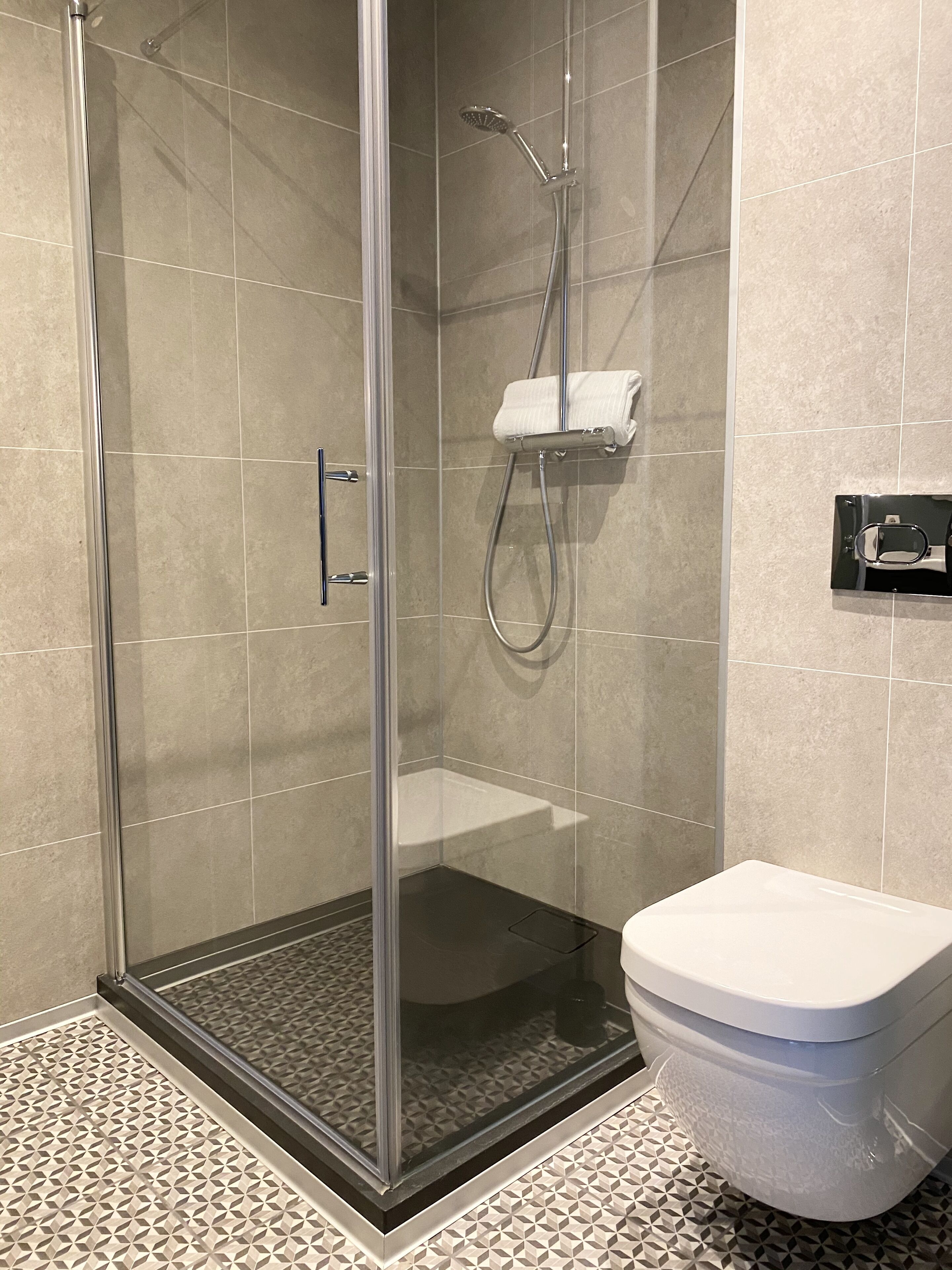 A modern bathroom with a glass-enclosed shower, a toilet, and a towel rack.
