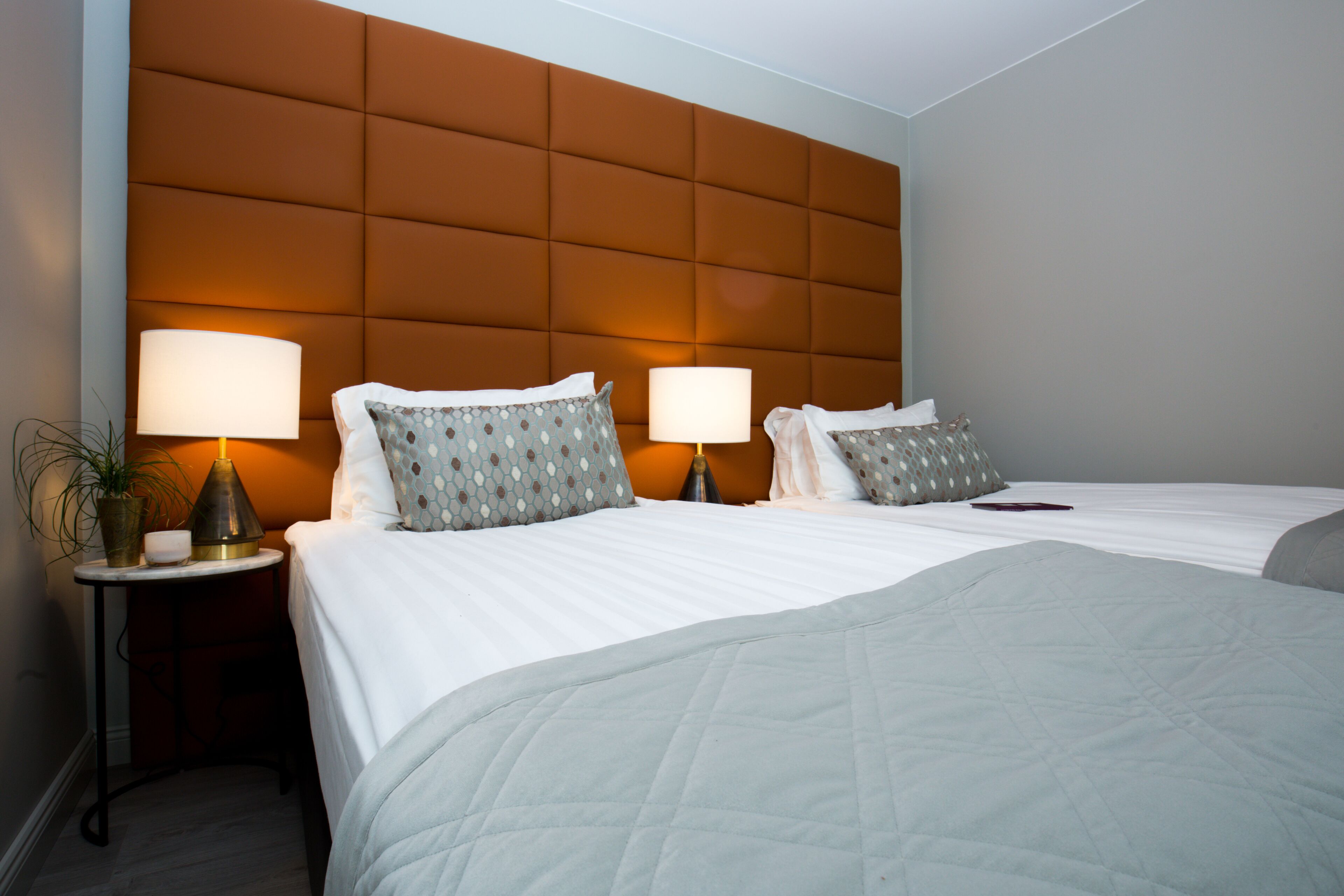 A hotel room with two beds, a padded headboard, bedside lamps, and a small table with a plant.