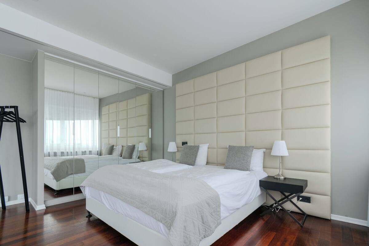 A modern bedroom with a large bed, a nightstand, a mirror, and a wardrobe.