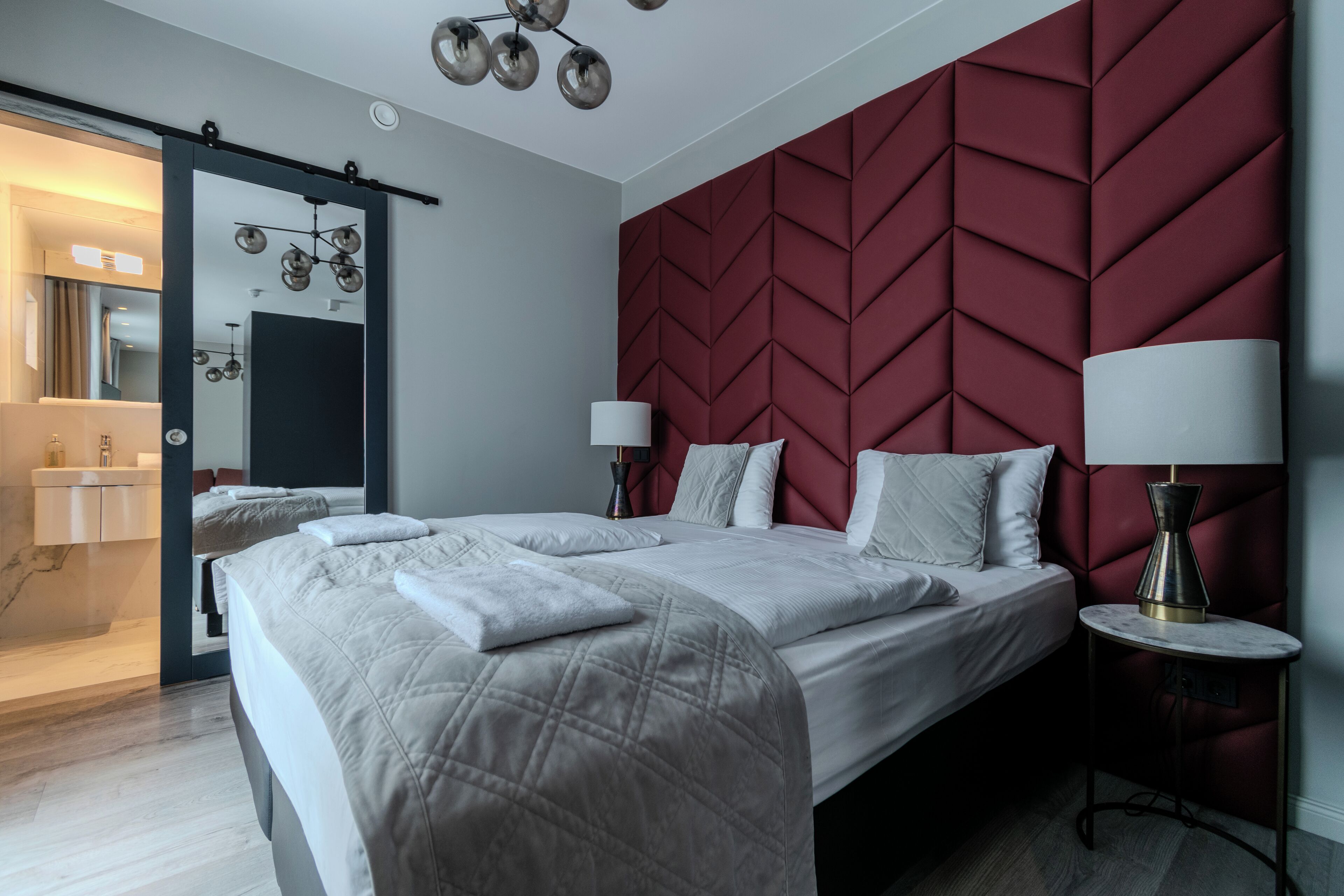 Una habitación de hotel moderna con una cama grande, un muro decorado en rojo y una puerta corredera que da a un baño.