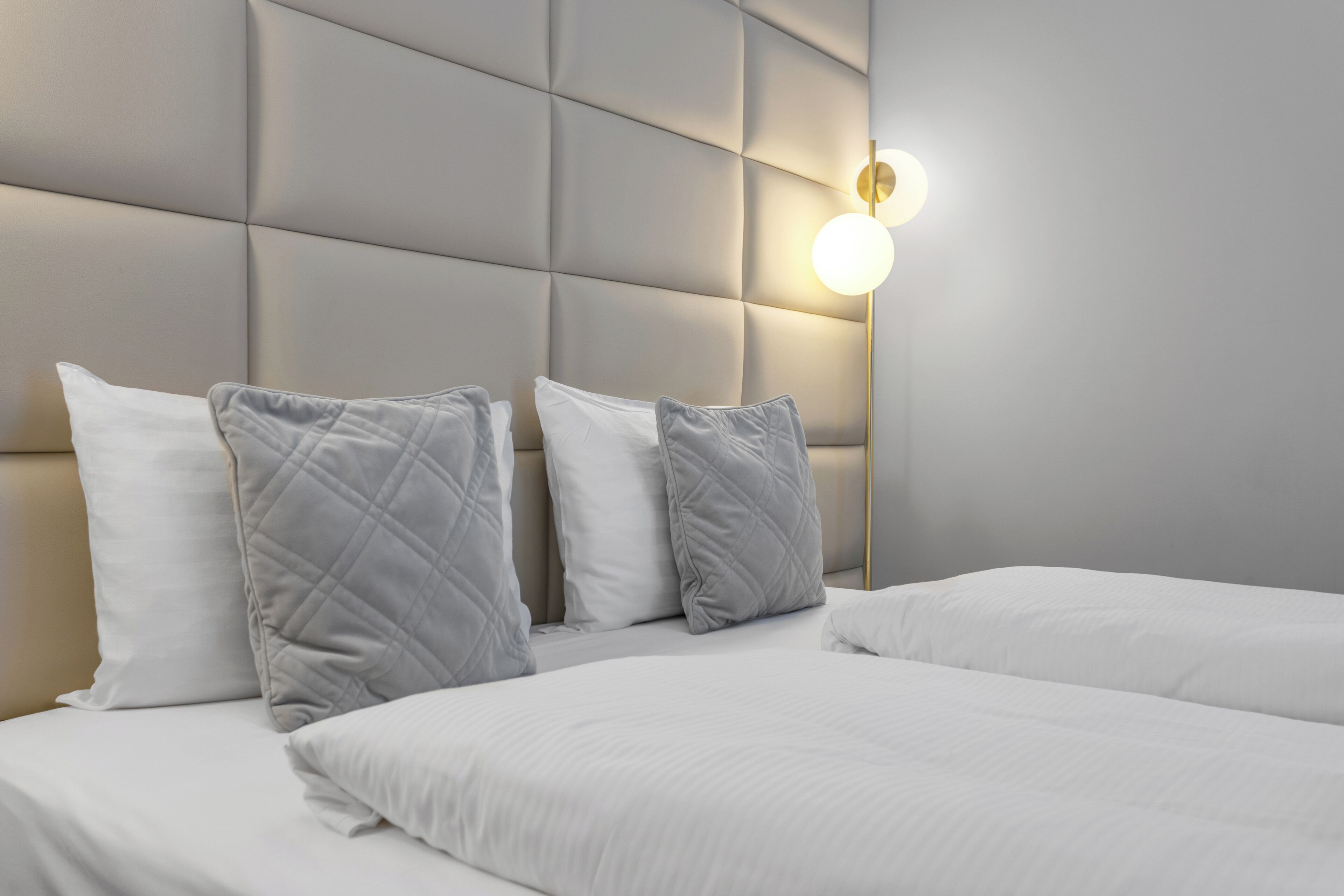 Une chambre d’hôtel avec une tête de lit capitonnée, deux lits avec du linge de lit blanc et un luminaire fixé au mur.