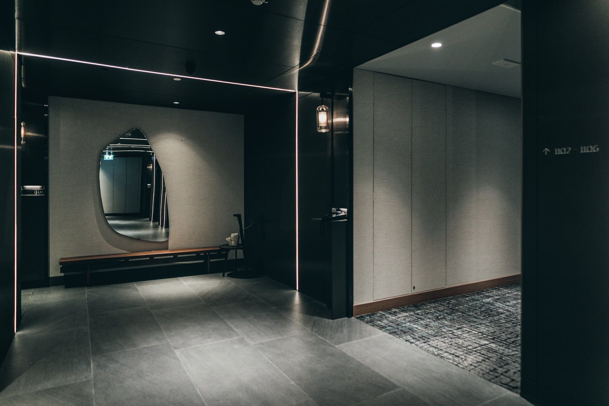Een moderne hotellobby met een grote spiegel, een bank en een receptiebalie.