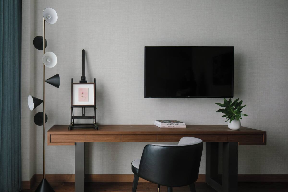 Ein modernes Zimmer mit einem Holztisch, einem schwarzen Stuhl, einer Stehlampe, einem gerahmten Bild, einem Buch mit dem Titel 'Wunderpflanzen' und einer Topfpflanze.