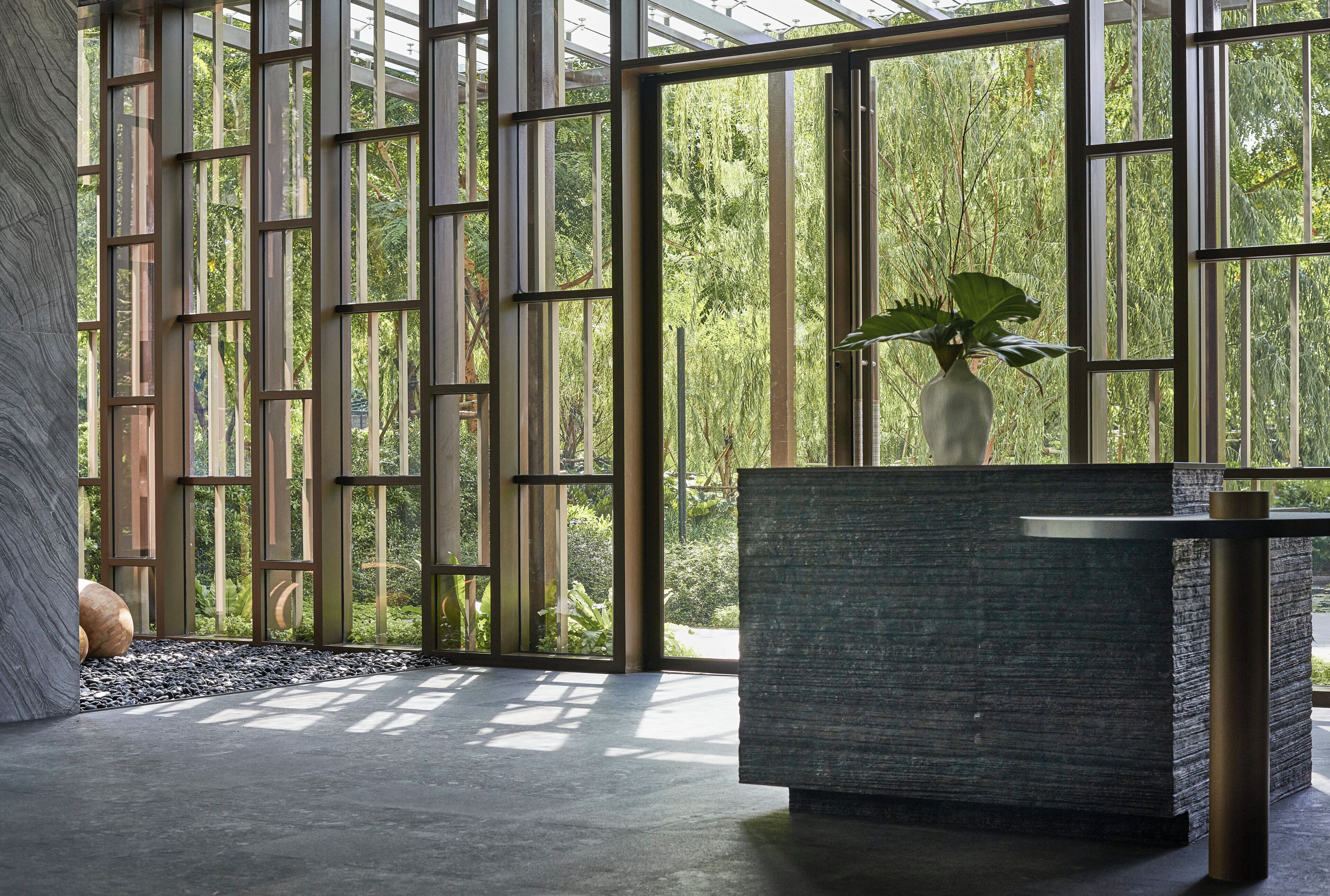 A modern interior with large windows, a stone wall, and a reception desk with a plant.