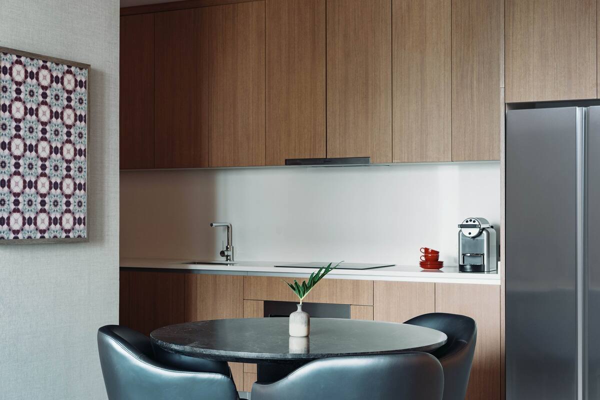 Eine moderne Küche mit Holzausbau, einem Edelstahlkühlschrank, einer Kaffeemaschine und einem Esstisch mit Stühlen.