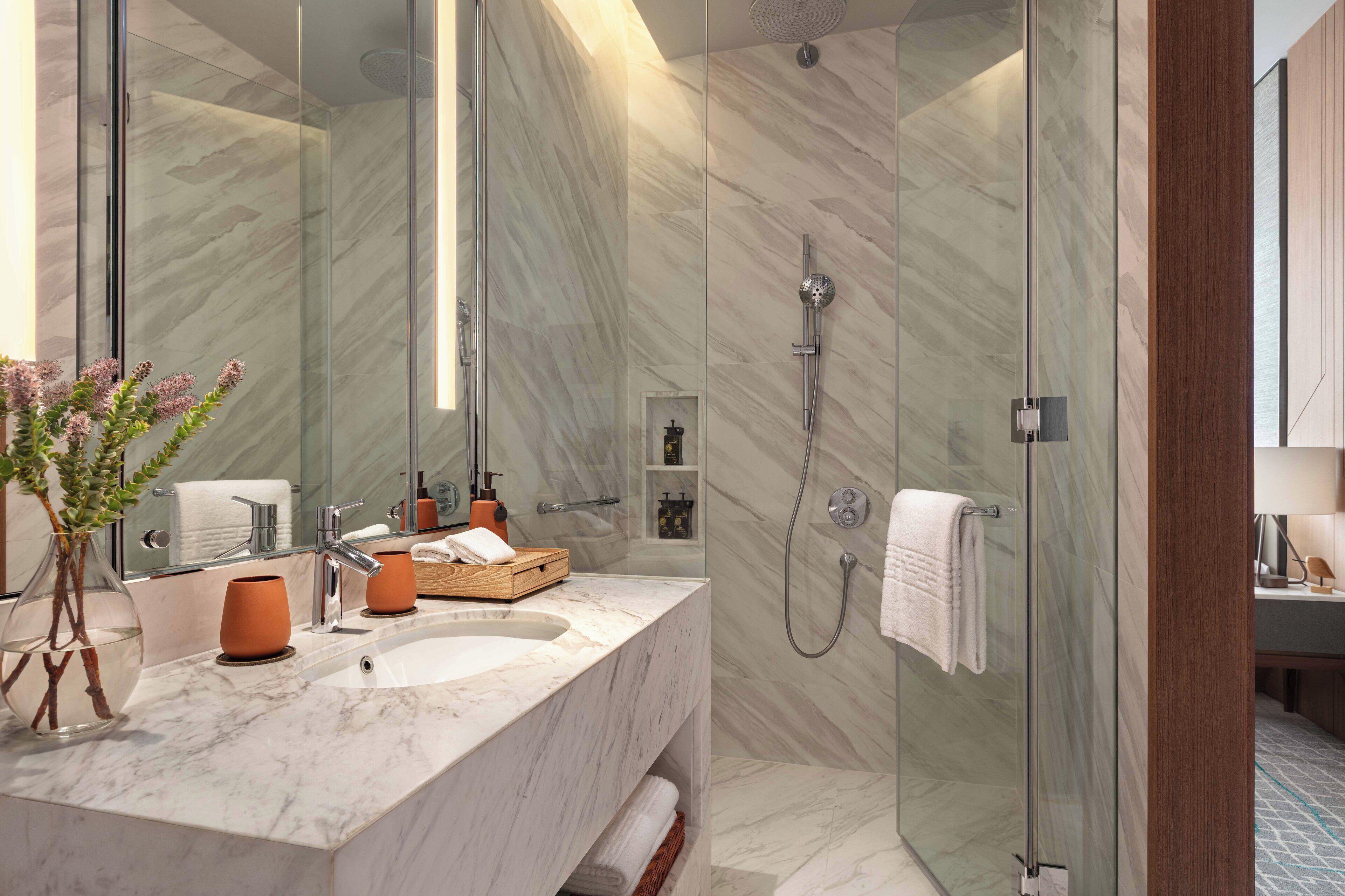 Un baño moderno con lavamanos de mármol, cabina de ducha de vidrio y un espejo grande.