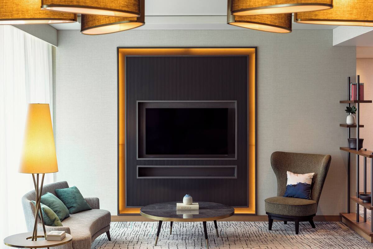 Ein modernes Wohnzimmer mit Flachbildfernseher, rundem Couchtisch, Sofa, Sessel und Stehlampe.
