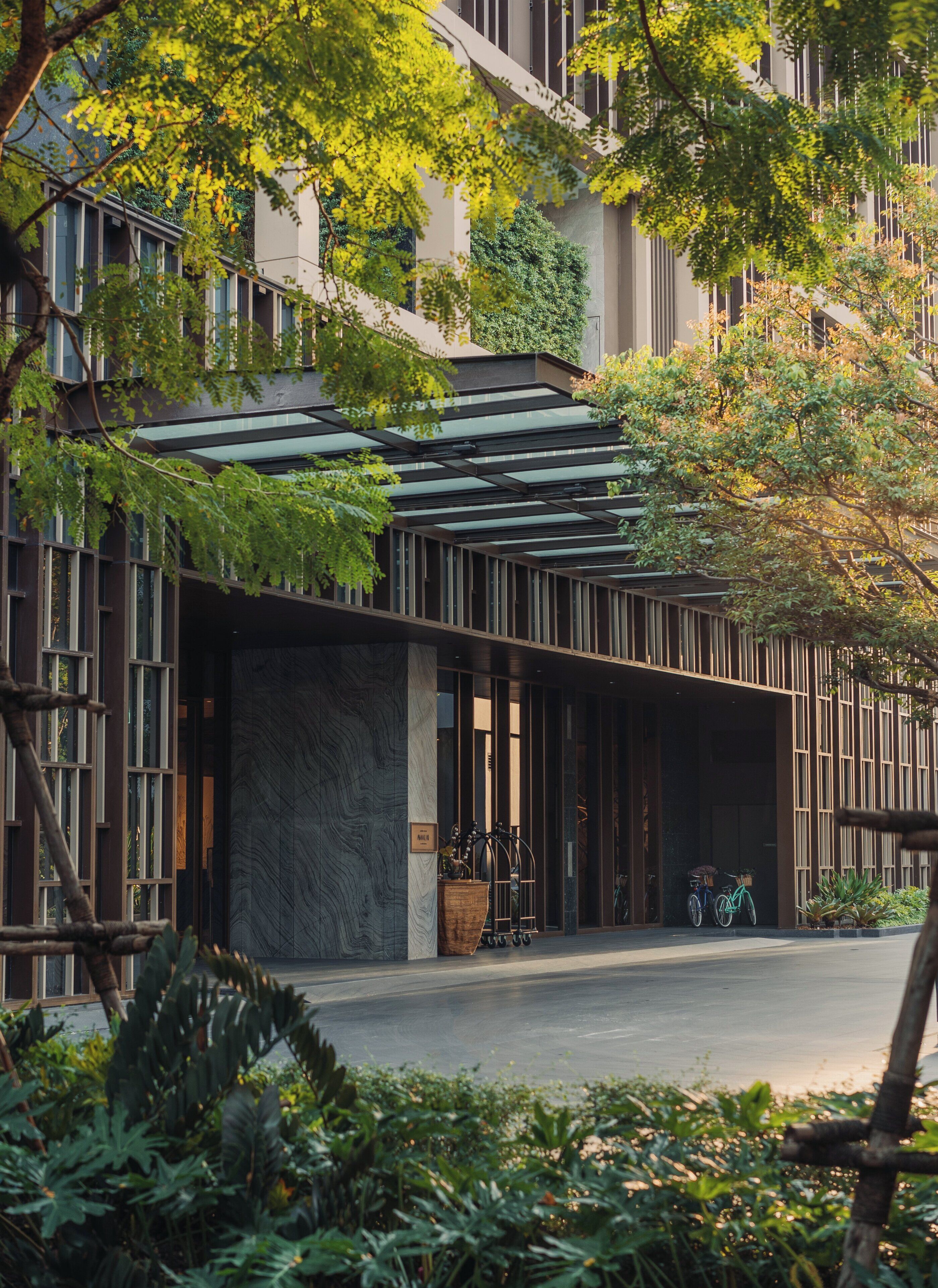 A modern building with a covered entrance, large windows, and greenery around.