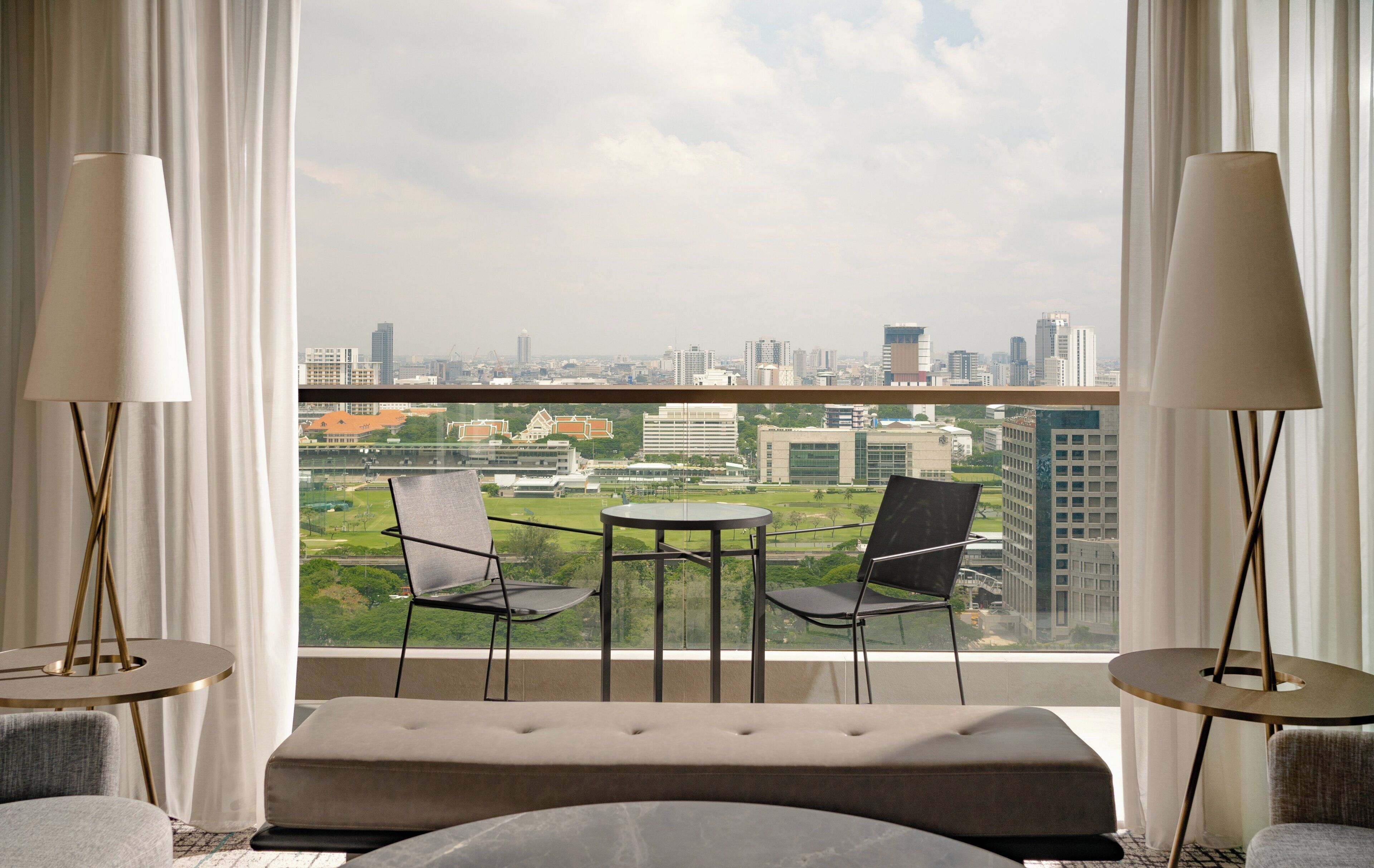 A modern hotel room with a balcony, two chairs, a small table, and a sofa.