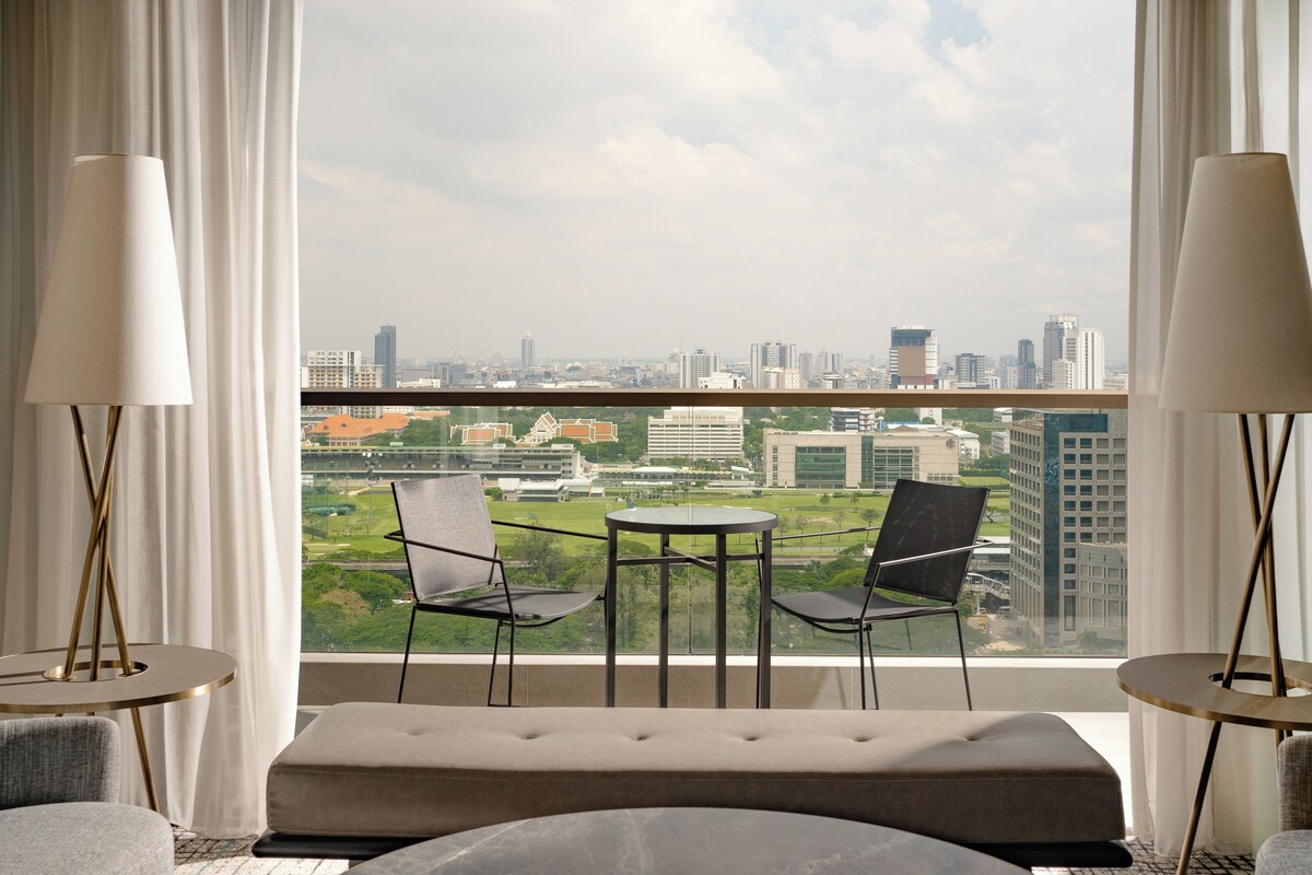 A room with a city view, two chairs, a round table, and a bench.