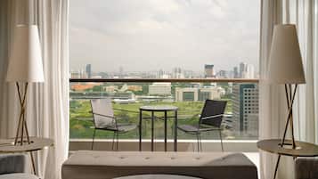 A modern hotel room with a balcony, two chairs, a small table, and a sofa.