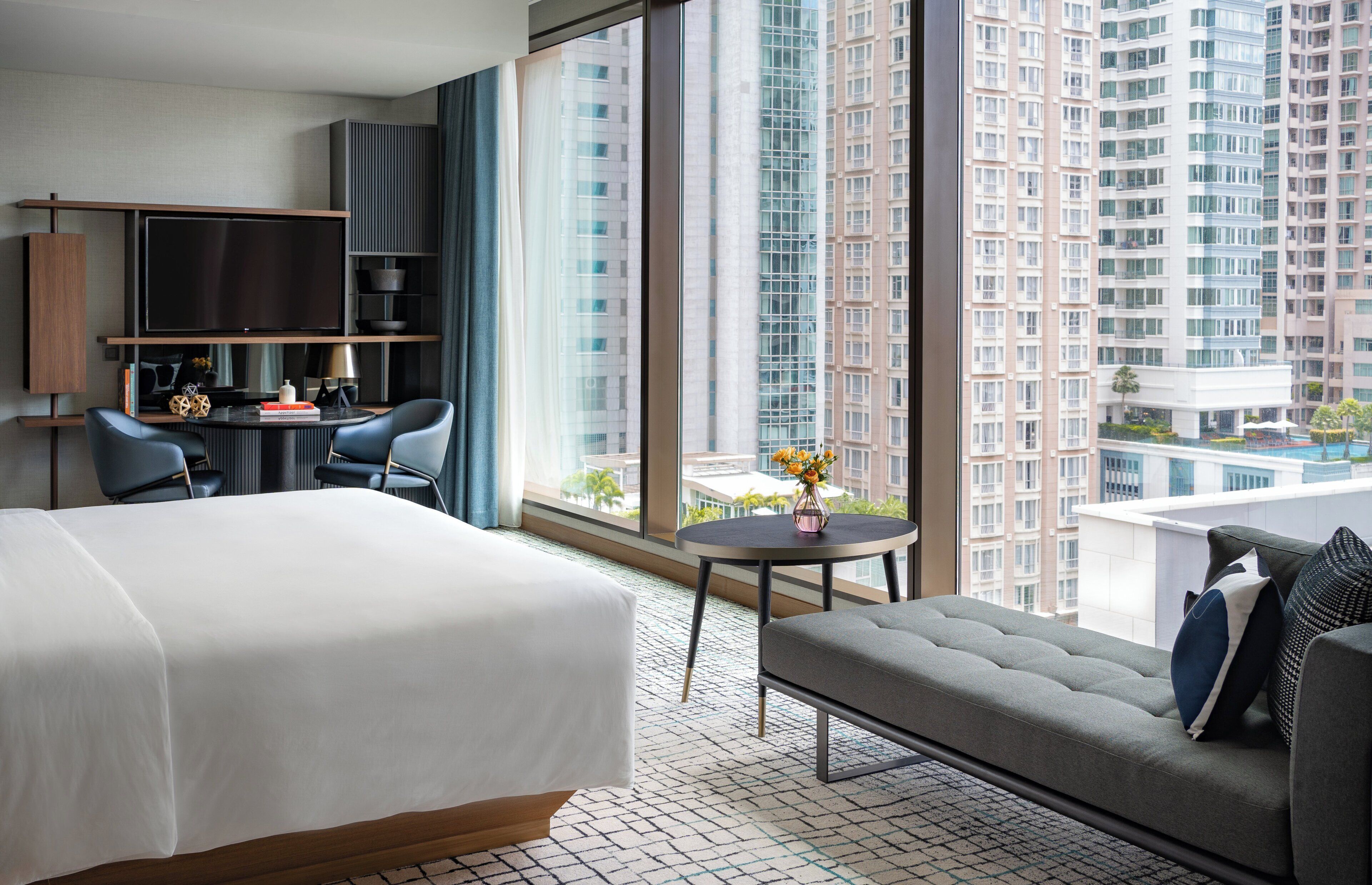 Une chambre d’hôtel comprenant un lit, un canapé, un bureau avec une chaise, une télévision et une grande fenêtre donnant sur la ville.