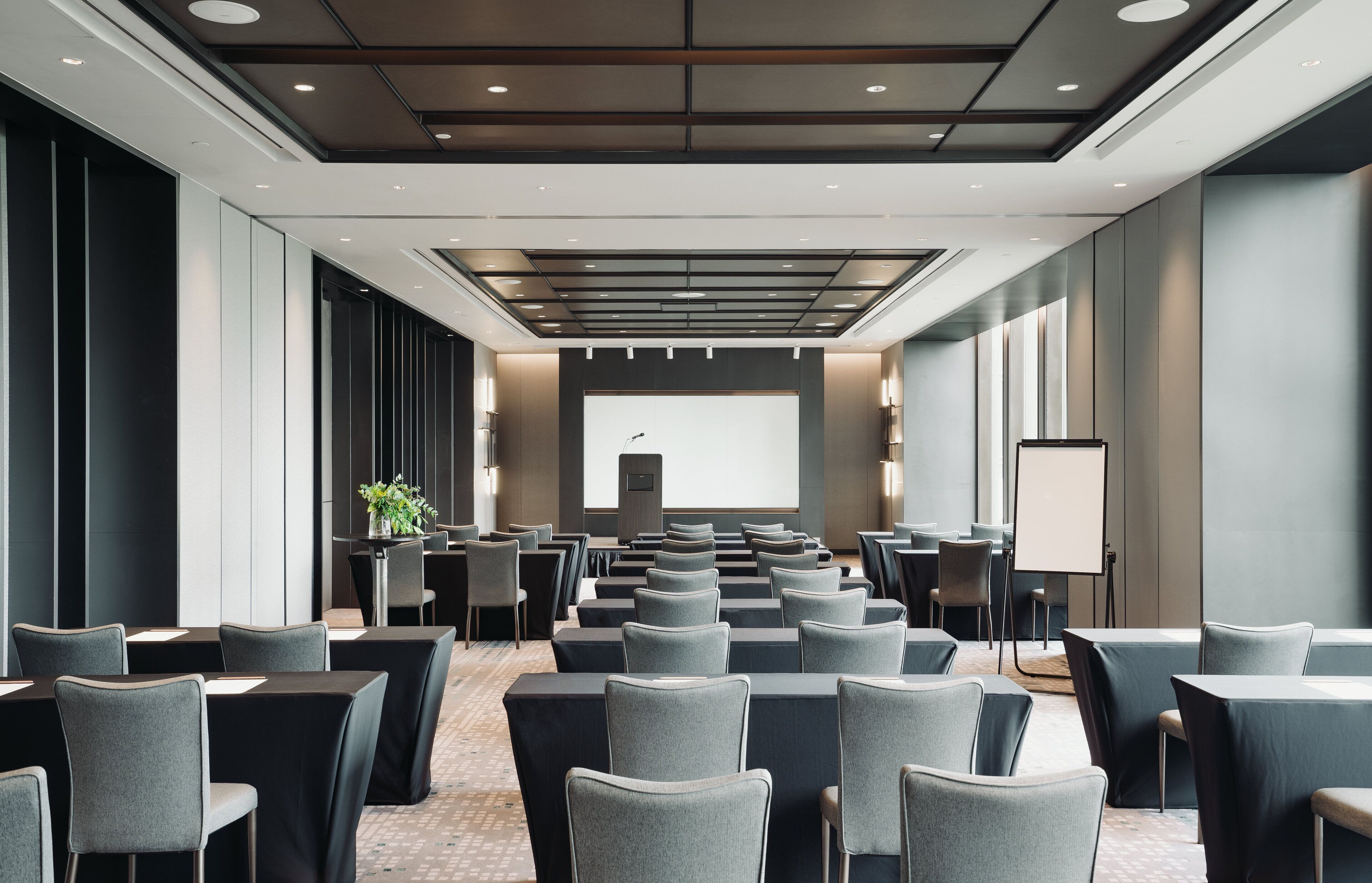 A conference room with rows of tables and chairs, a projector screen, and a presentation podium.