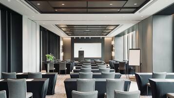 A conference room with rows of tables and chairs, a projector screen, and a presentation podium.