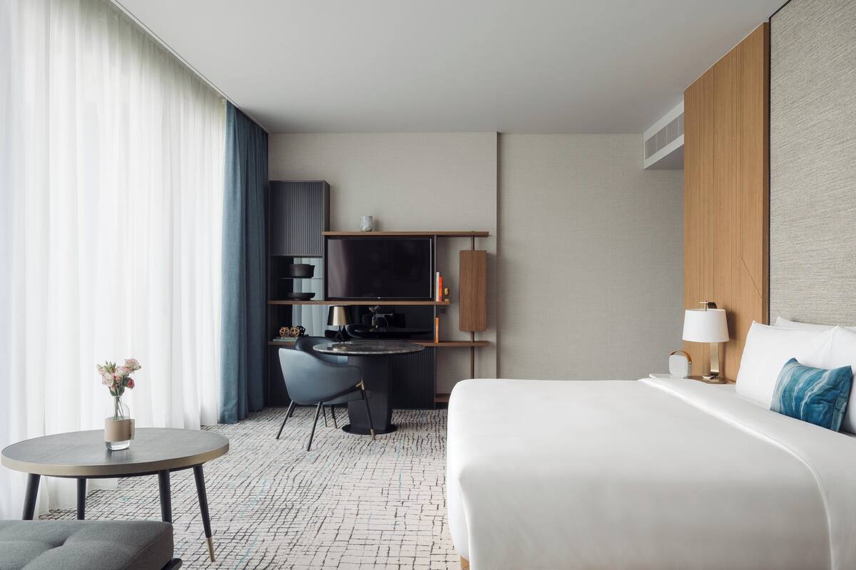 Ein modernes Hotelzimmer mit Bett, Schreibtisch, Stuhl, Nachttisch und Fernseher.