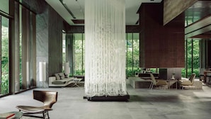Un vaste espace de vie agrémenté d’un lustre moderne, de sièges confortables et de grandes fenêtres offrant une vue sur la verdure.