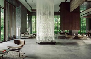 Un vaste espace de vie agrémenté d’un lustre moderne, de sièges confortables et de grandes fenêtres offrant une vue sur la verdure.